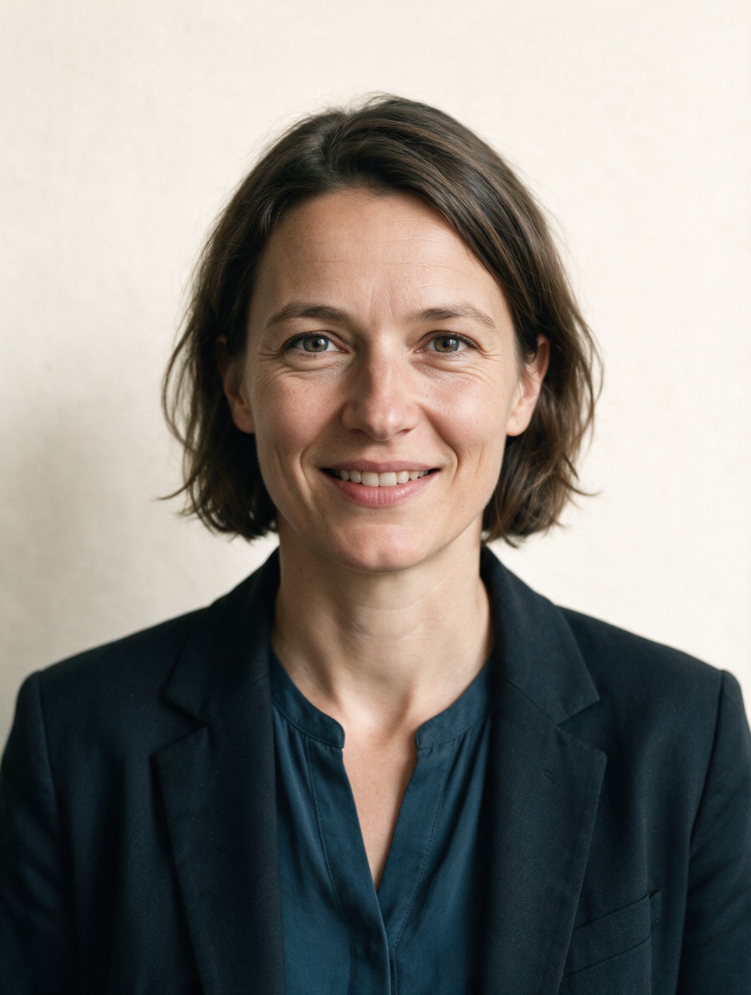 Porträt einer Frau in dunklem Blazer vor hellem Hintergrund, freundlicher Blick
